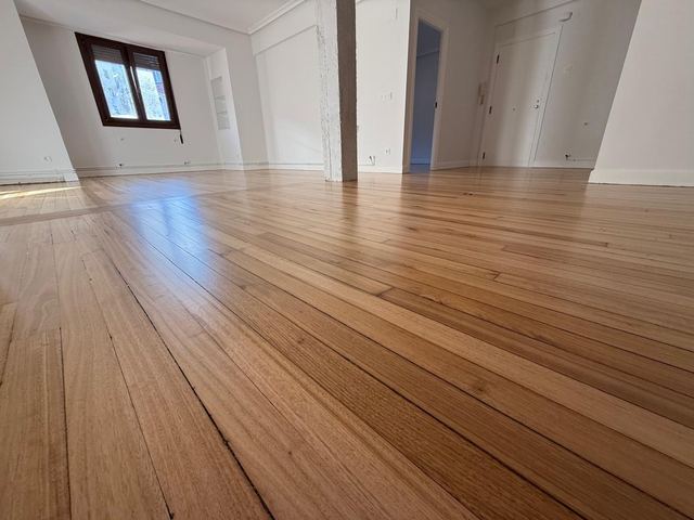Salón amplio con tarima clara recién lijada y barnizada